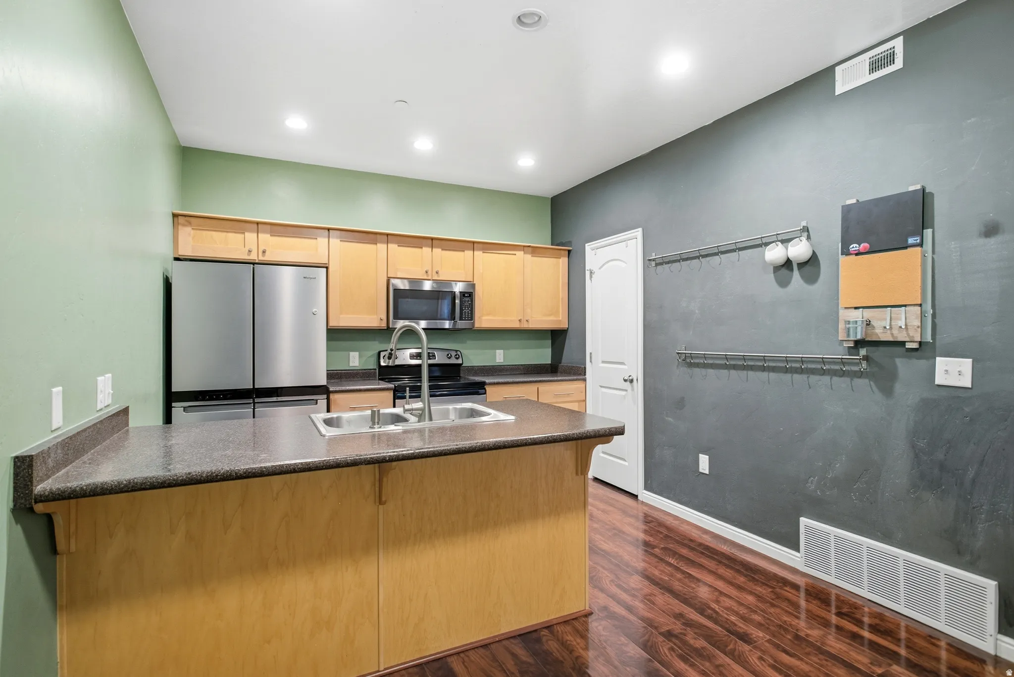 Kitchen with a peninsula, stainless steel appliances, dark wood-style flooring, light wood finish cabinetry, and recessed lighting