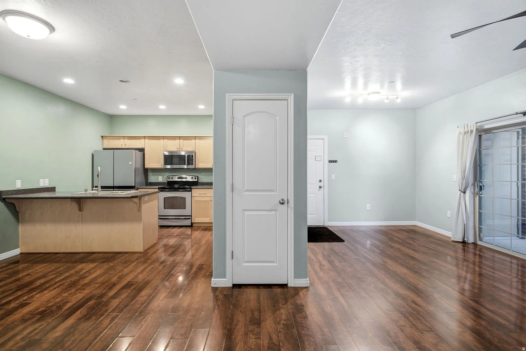 Kitchen featuring a kitchen bar, stainless steel appliances, a peninsula, dark countertops, and dark wood finished floors