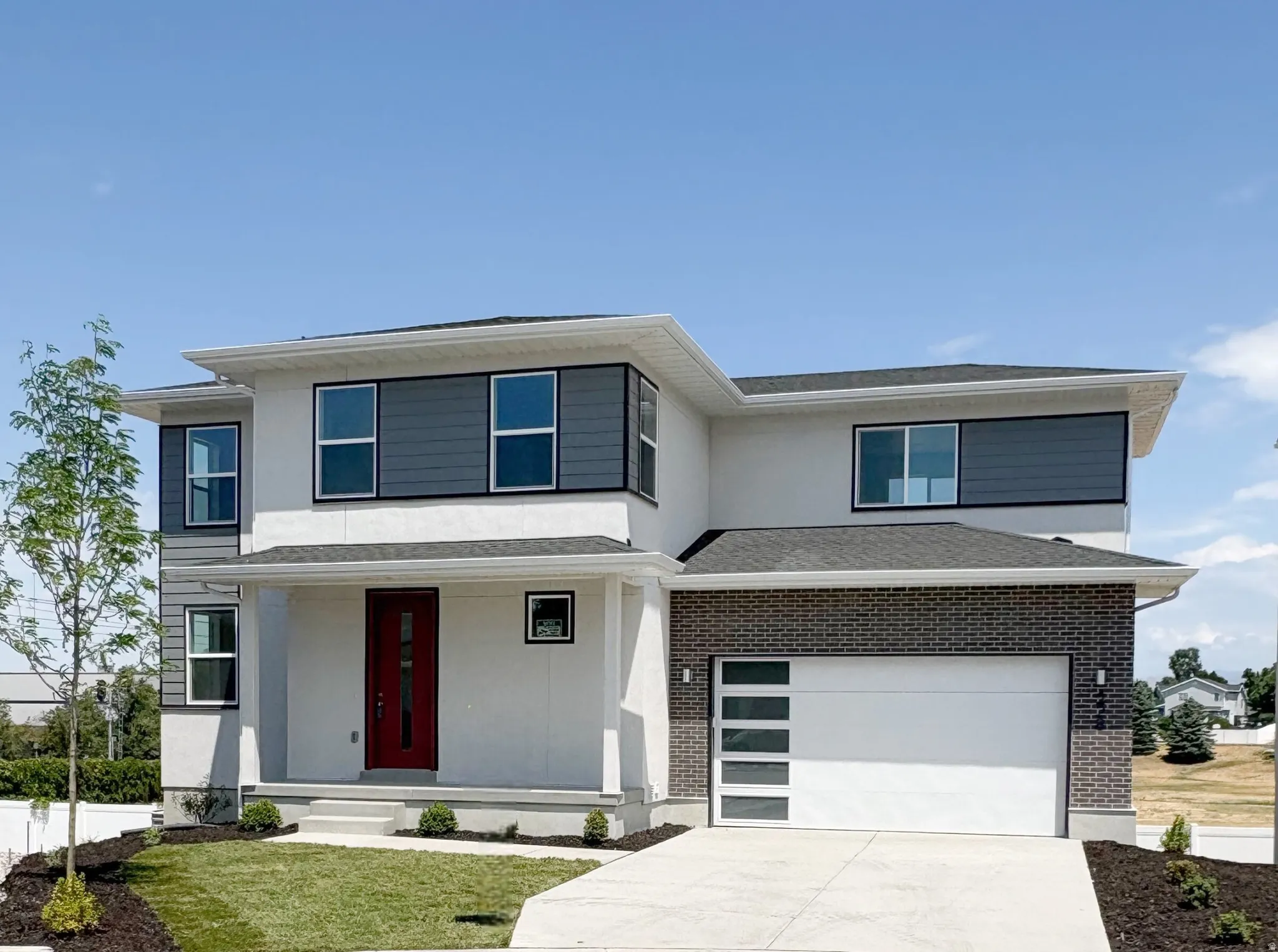 Contemporary two-story residence featuring a white stucco exterior with dark gray horizontal siding accents and dark brick veneer
