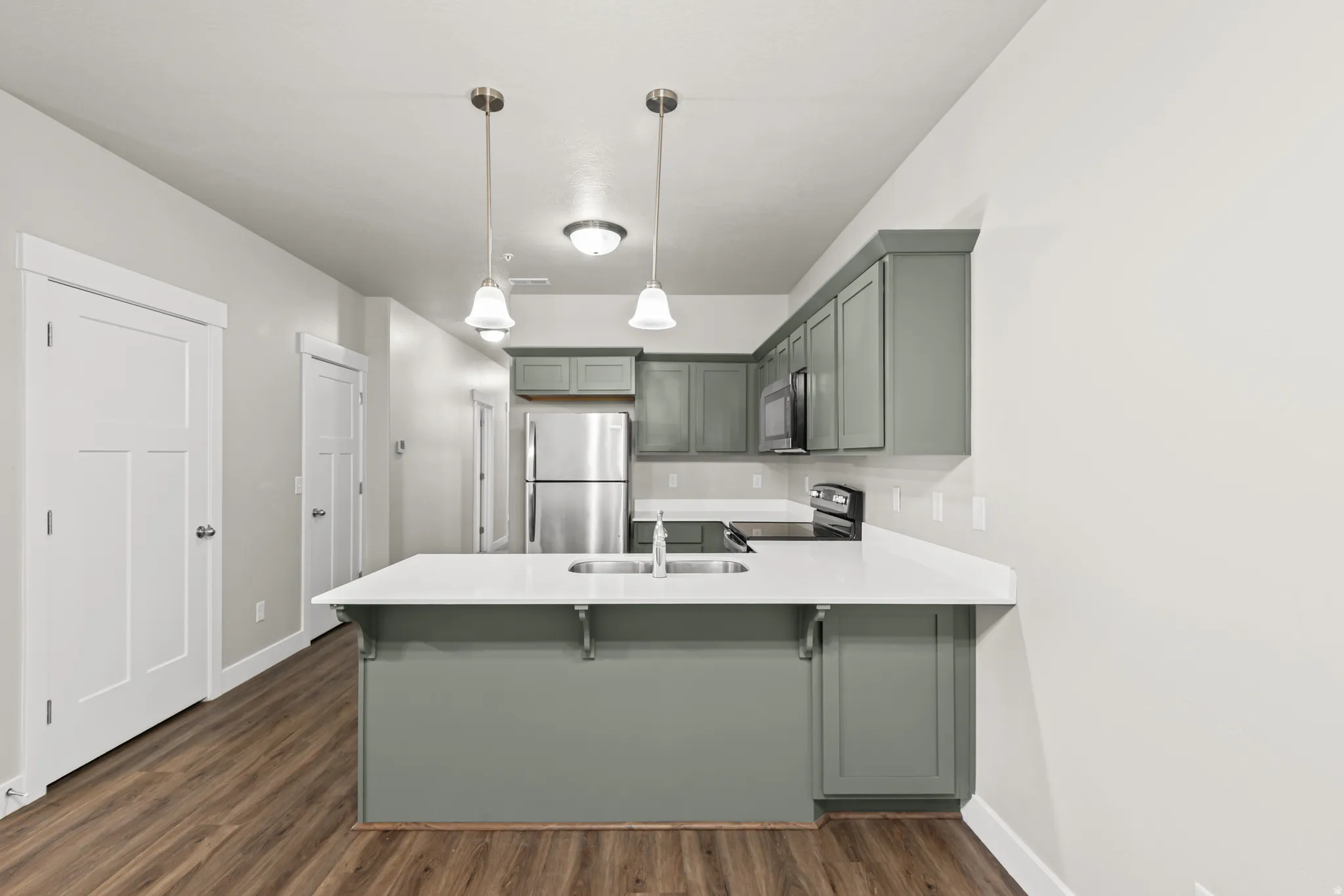 Kitchen featuring a peninsula, stainless steel appliances, hanging light fixtures, green cabinets, and a breakfast bar area