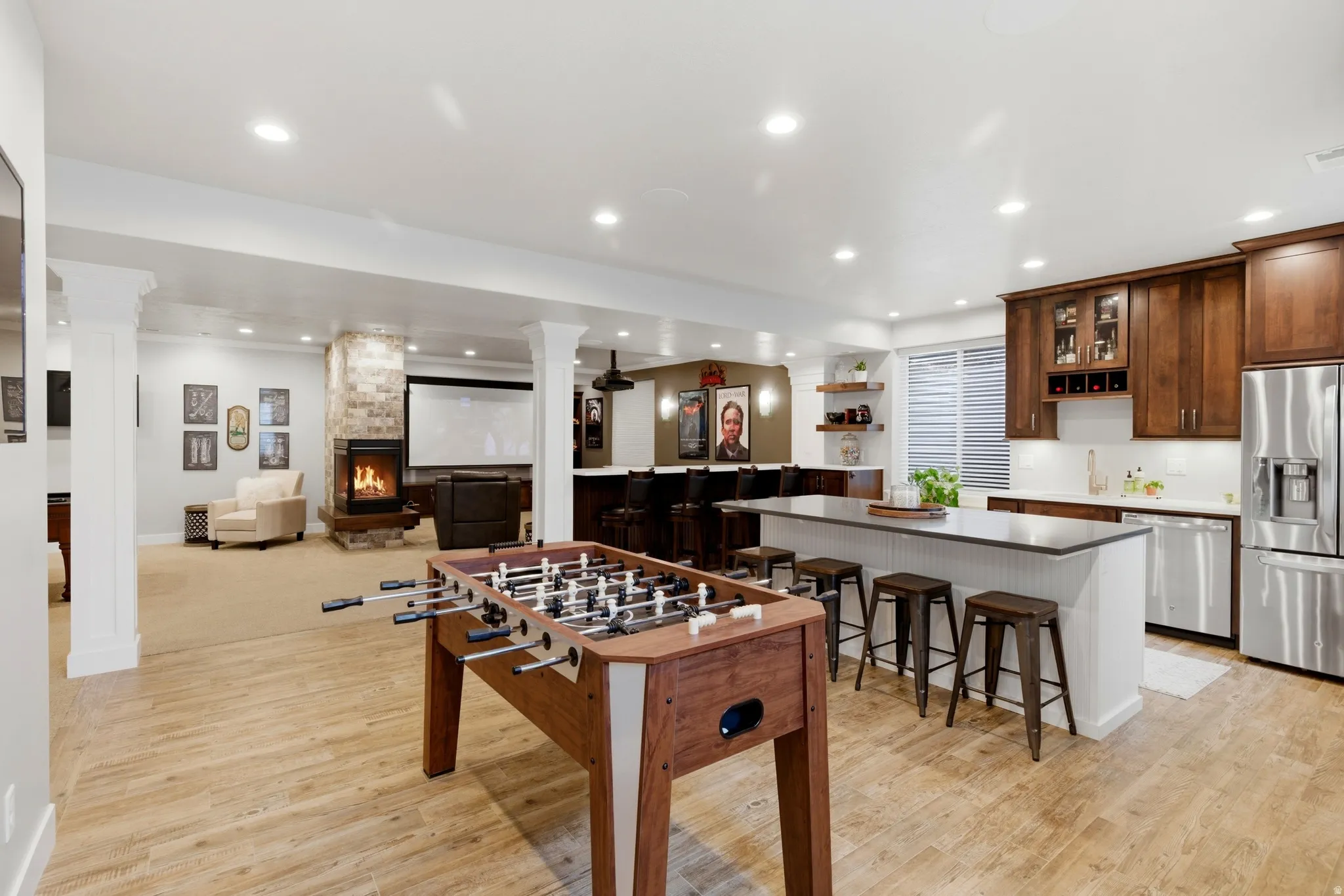 Game room featuring light wood-style floors, ornate columns, a stone fireplace, recessed lighting, and bar with sink