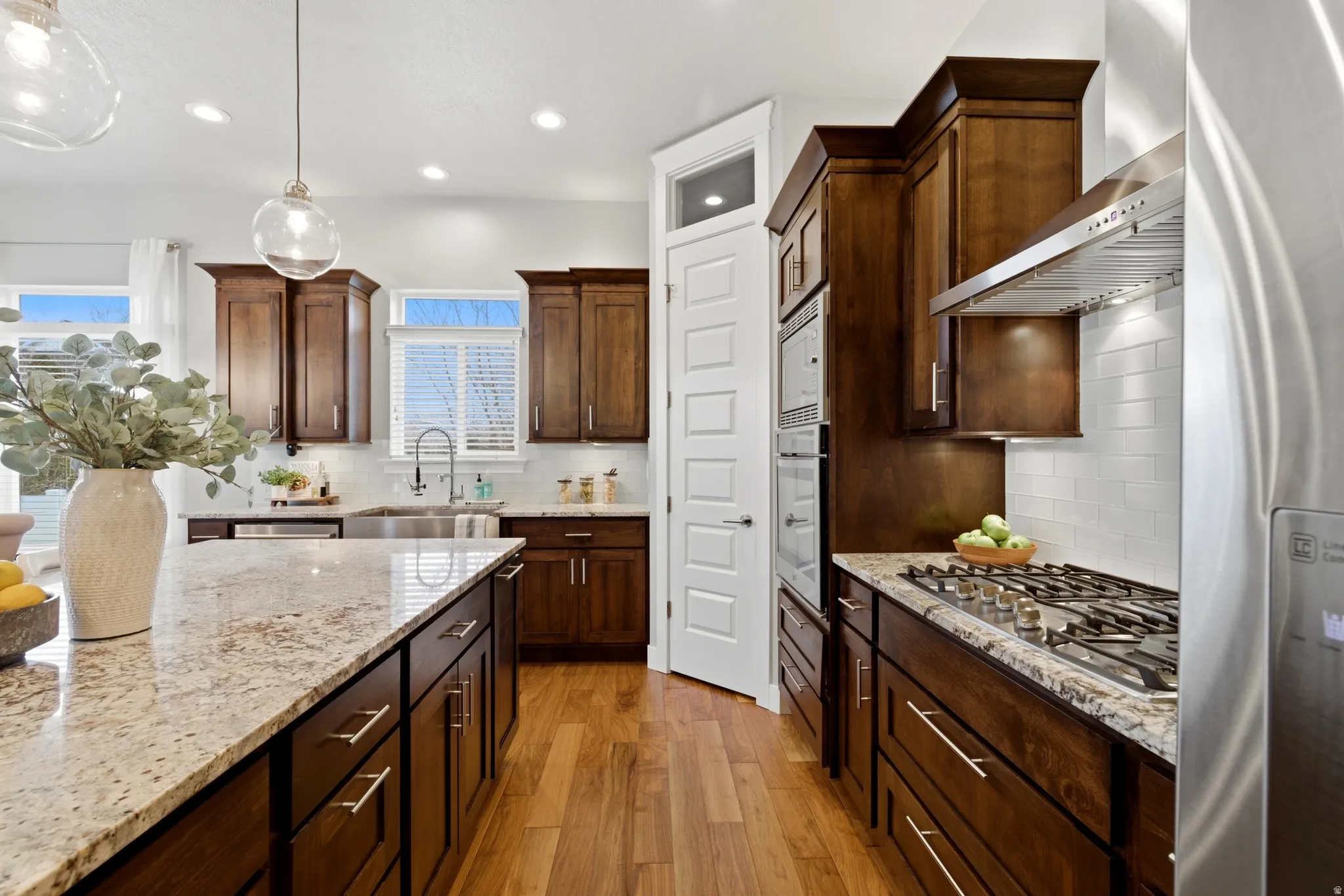 Kitchen with stainless steel appliances, light stone counters, decorative backsplash, and light wood-style flooring