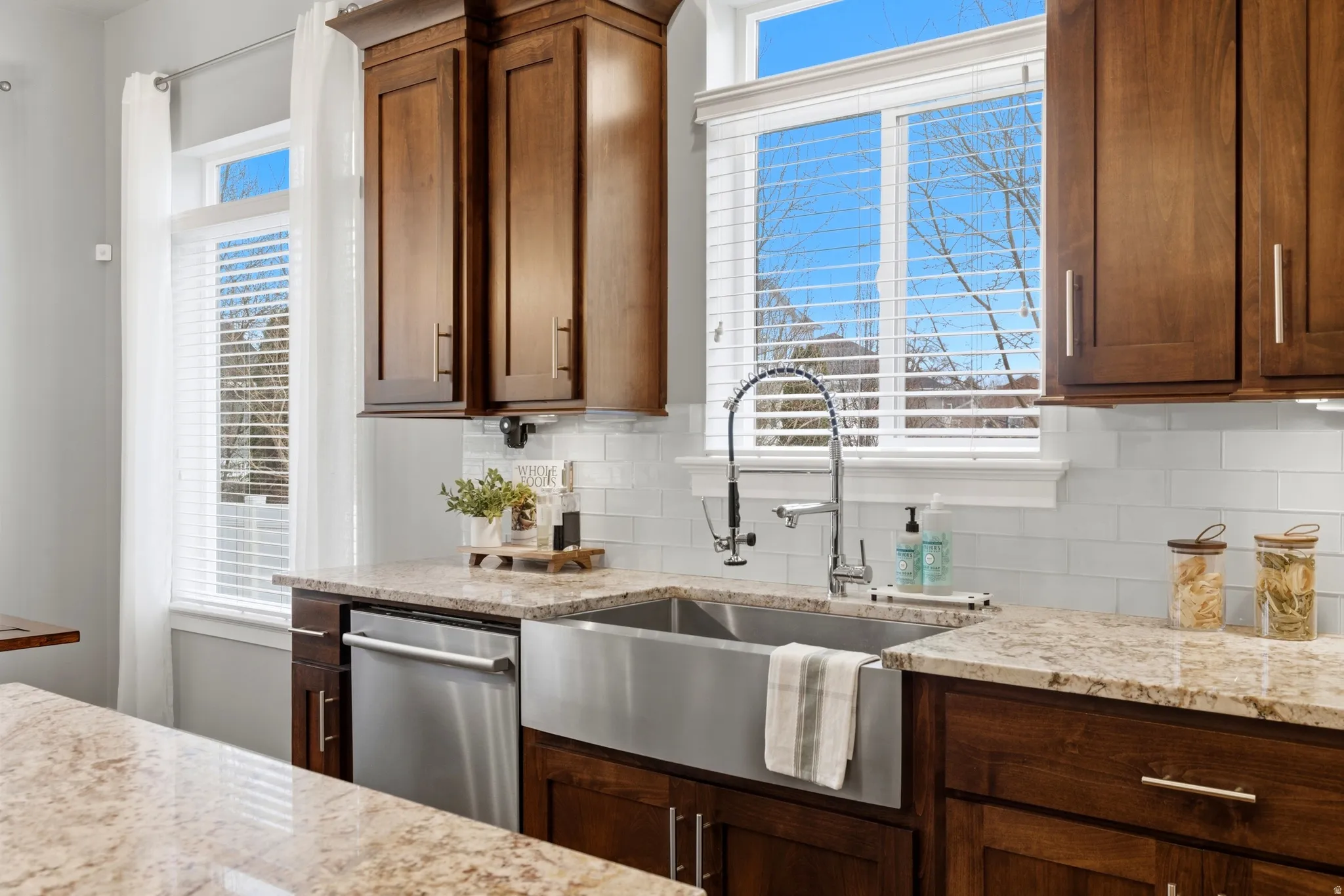 Kitchen with tasteful backsplash, light stone counters, dishwasher, and plenty of natural light