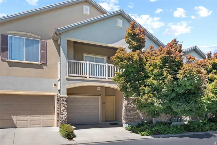 View of front of house featuring a balcony, stucco siding, an attached garage, and driveway