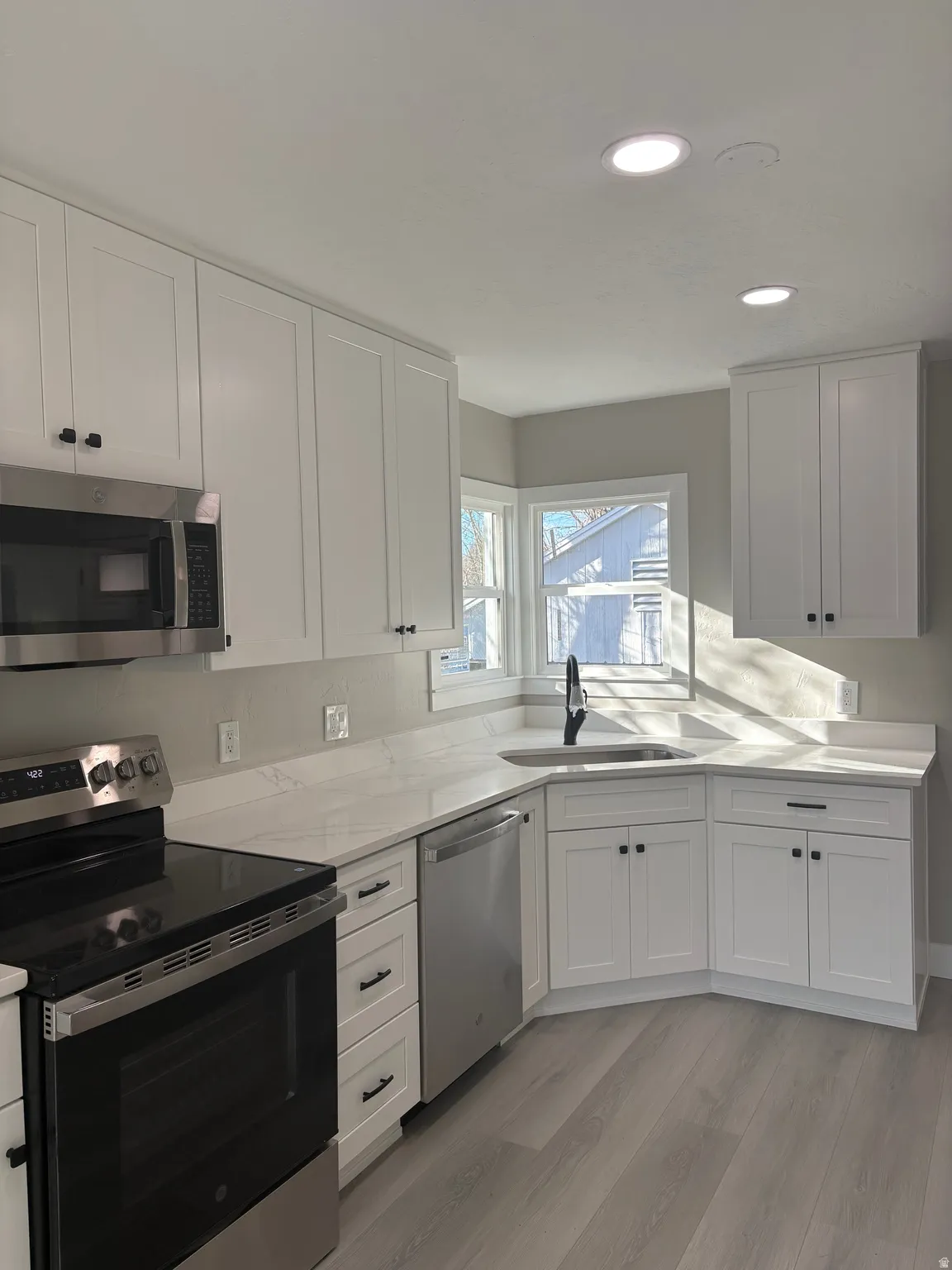 Kitchen featuring stainless steel appliances, white cabinetry, recessed lighting, light wood-type flooring, and light stone countertops