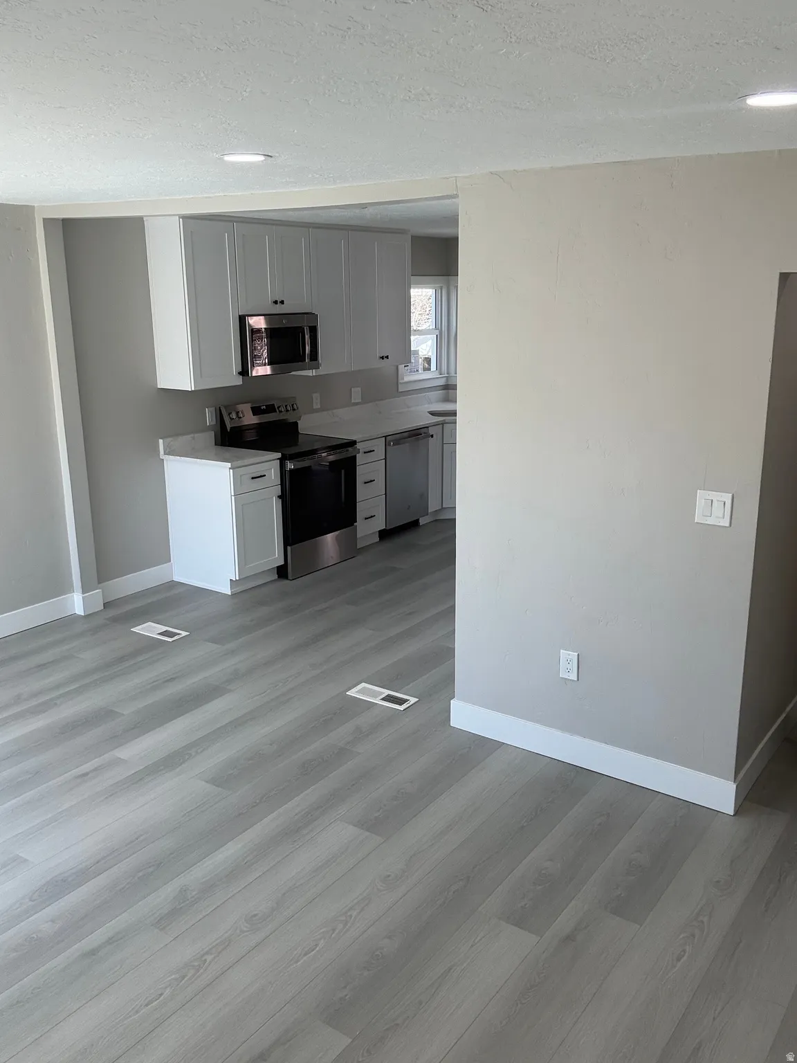 Kitchen featuring stainless steel appliances, white cabinetry, a textured ceiling, and light laminate flooring