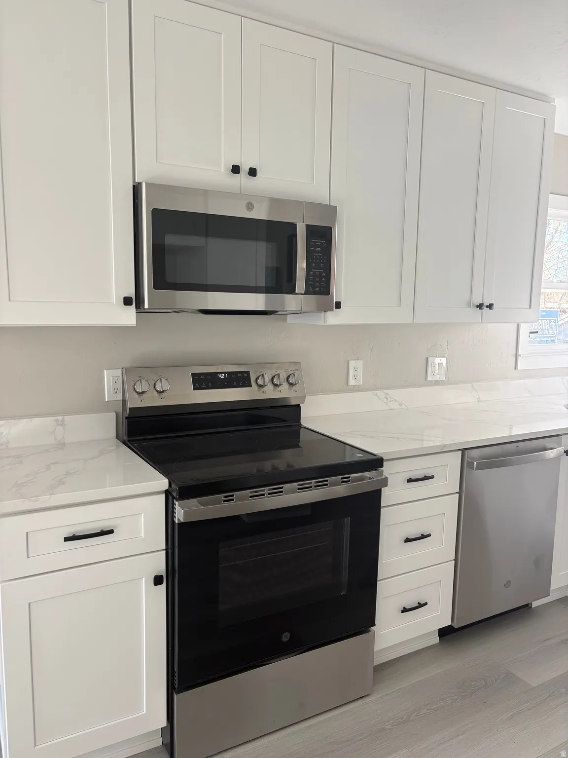 Kitchen with stainless steel appliances, light stone countertops, and white cabinetry