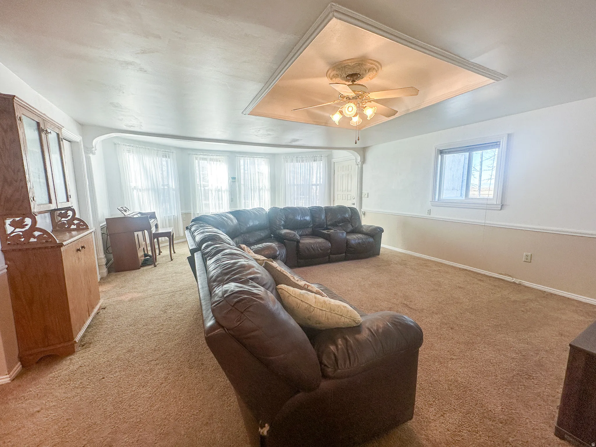 Carpeted living room featuring a raised ceiling and a ceiling fan