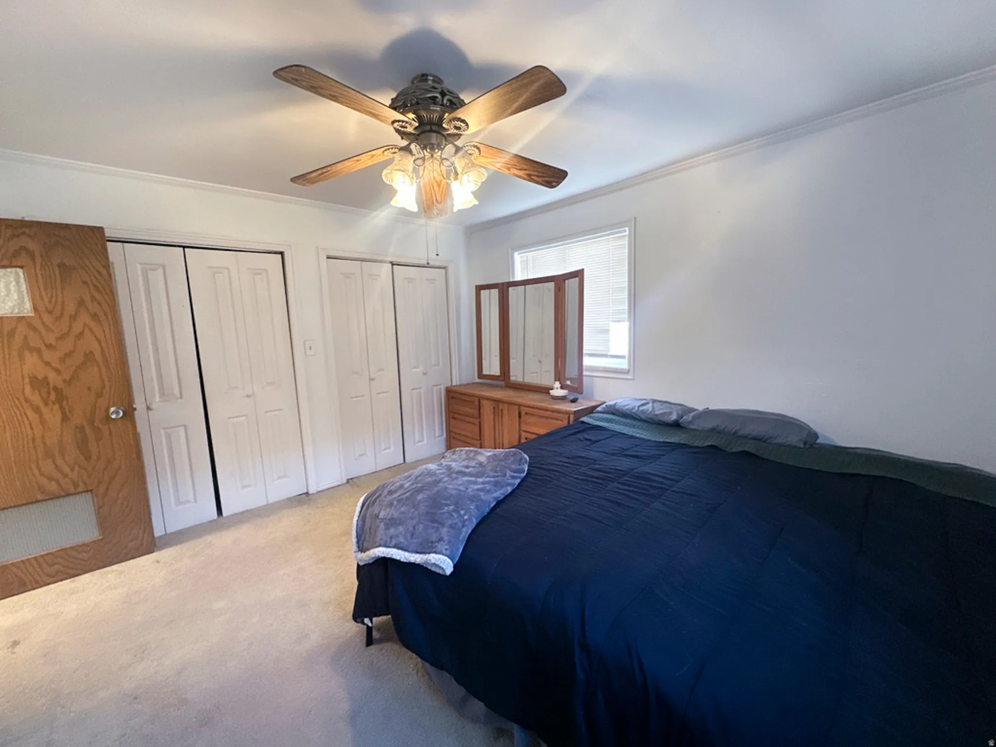 Carpeted bedroom featuring ornamental molding, two closets, and a ceiling fan