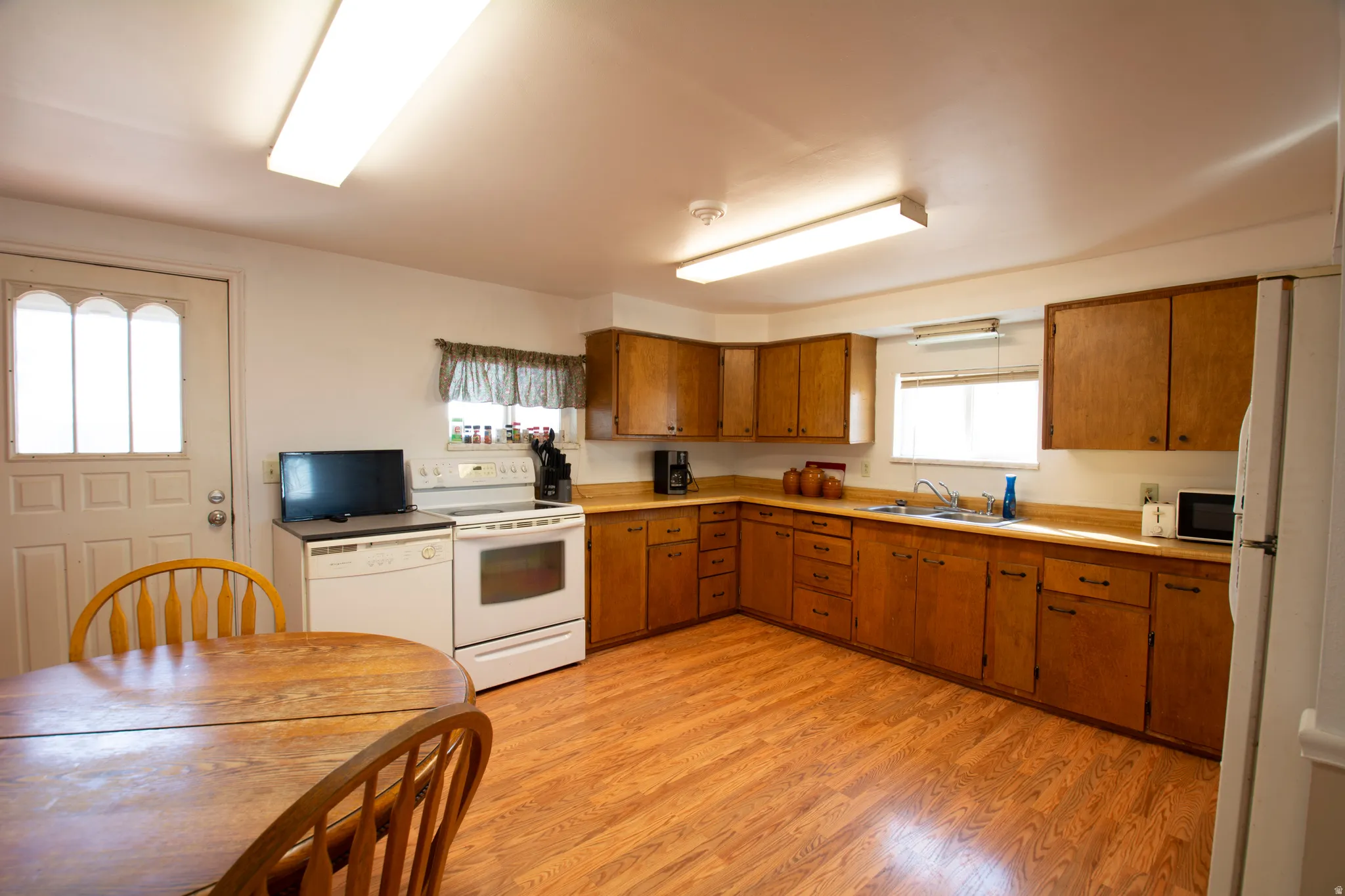 Kitchen with white appliances, wood finish cabinetry, light countertops, light wood-type flooring, and plenty of natural light