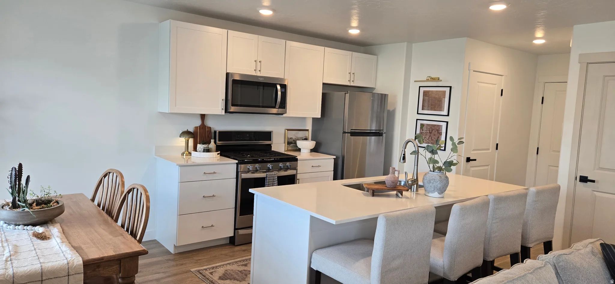 Kitchen featuring stainless steel appliances, white cabinetry, an island with sink, a kitchen breakfast bar, and dark wood-type flooring
