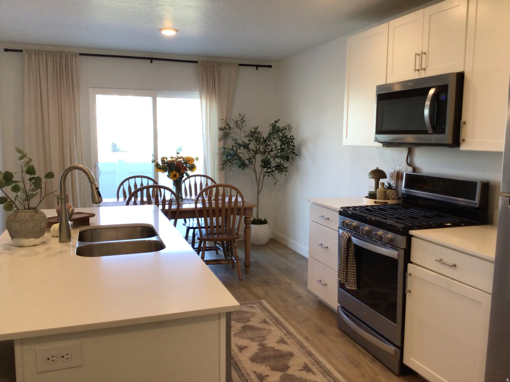 Kitchen featuring stainless steel appliances, white cabinets, light wood finished floors, and a kitchen island with sink