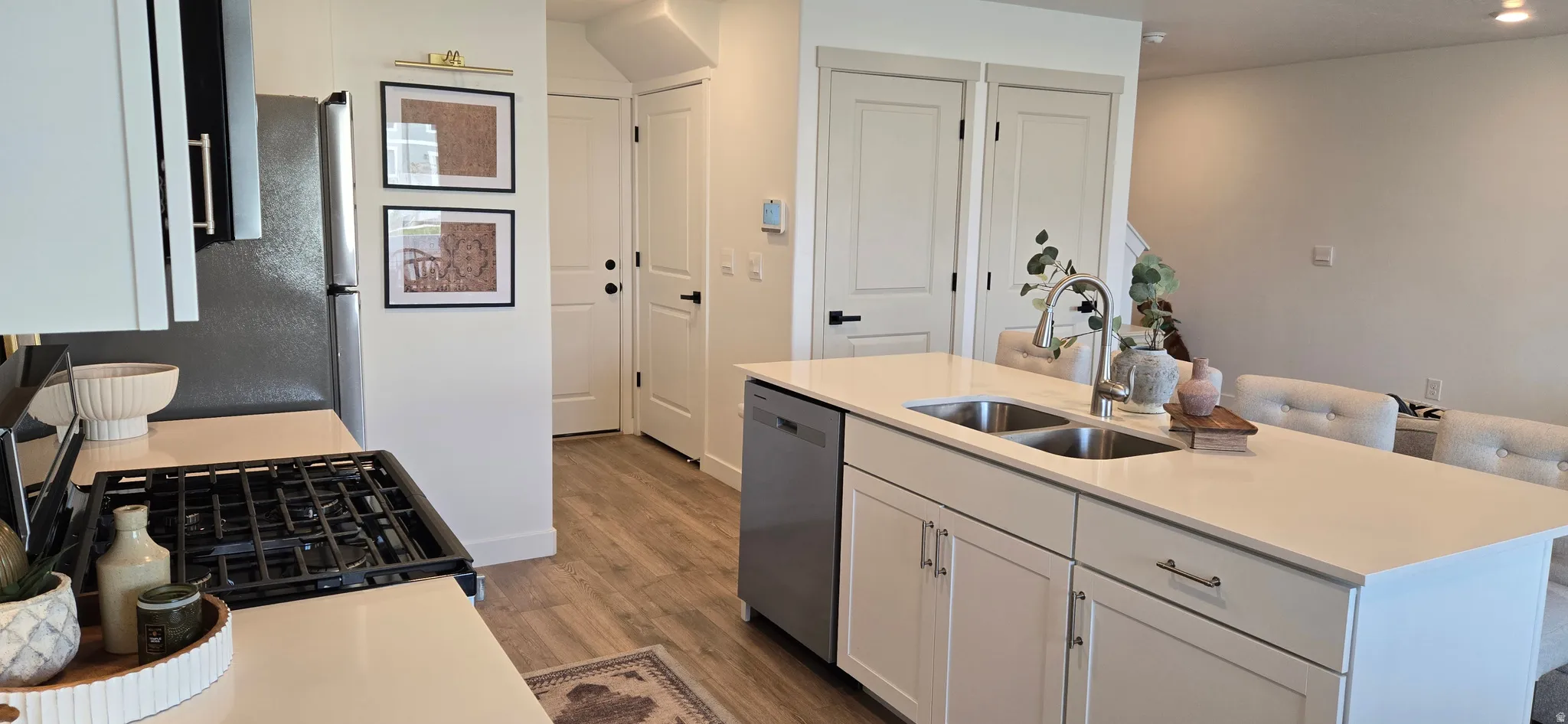 Kitchen with gas stove, white cabinetry, dishwasher, dark wood-type flooring, and a center island with sink