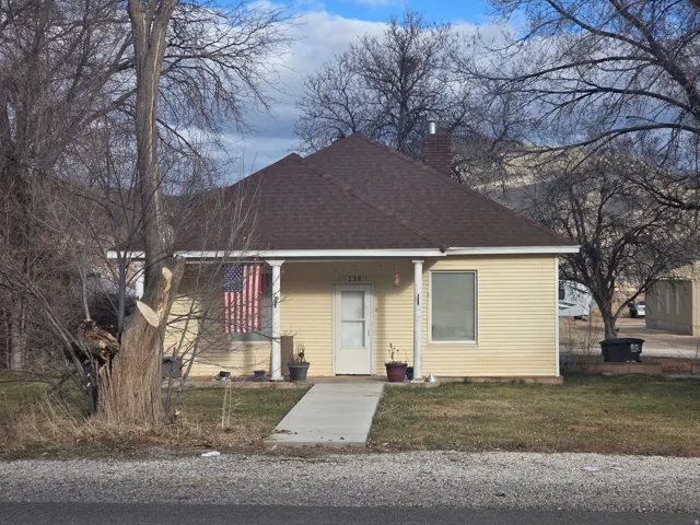 View of front facade with a porch, a front lawn, roof with shingles, and a chimney