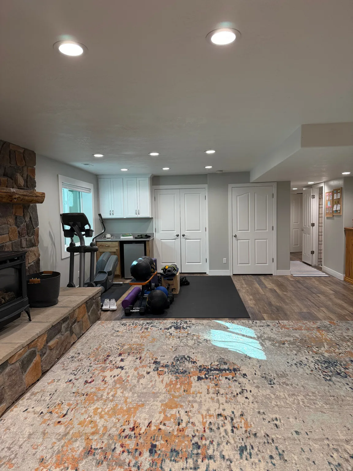 View of the basement showing the secondary laundry room doors, mini fridge, workout space, and linen closet.