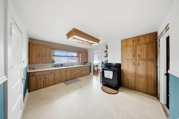 Kitchen featuring light flooring, black / electric stove, light countertops, and wood finish cabinetry