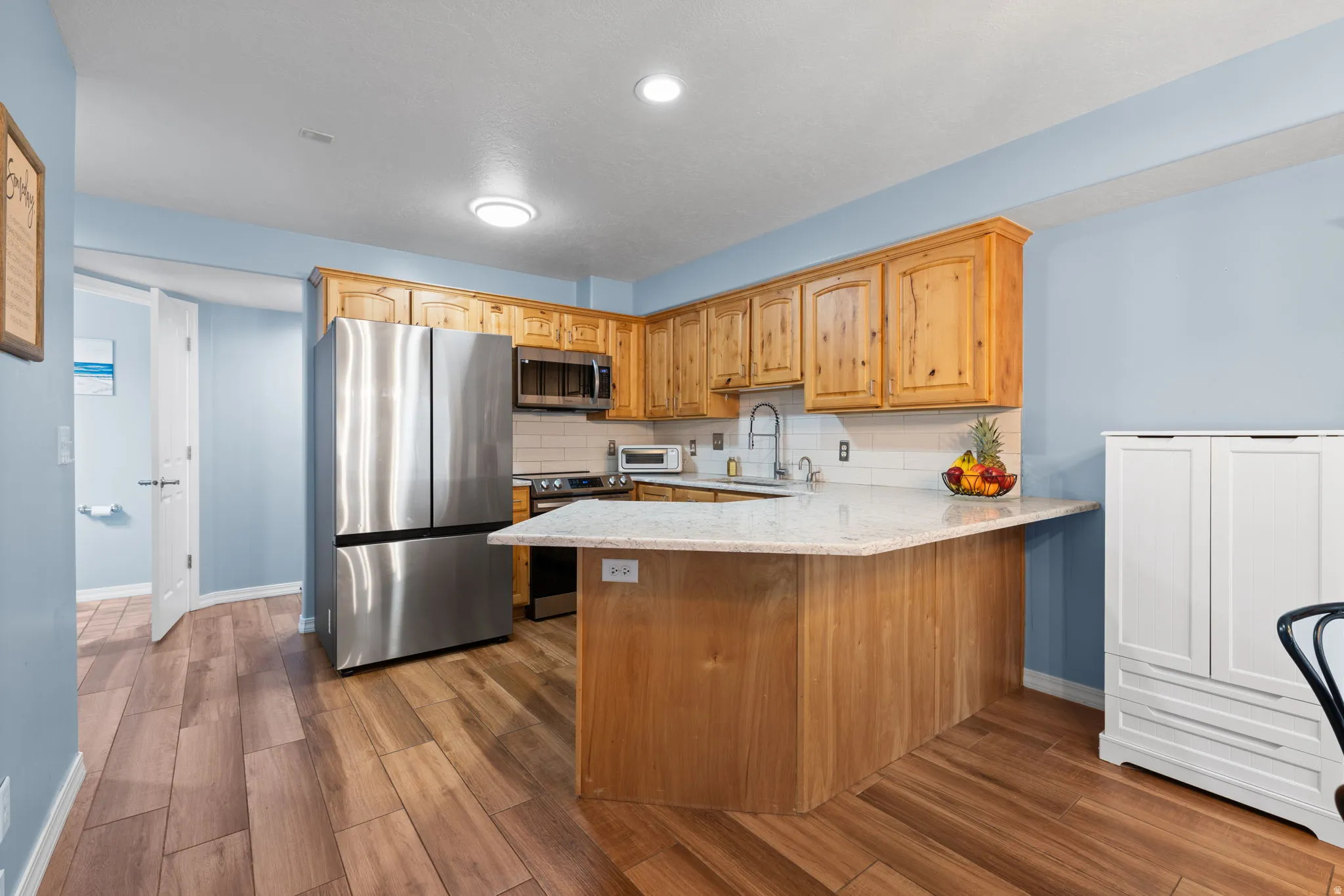Kitchen featuring stainless steel appliances, tasteful backsplash, light stone counters, a peninsula, and ceramic wood tile flooring