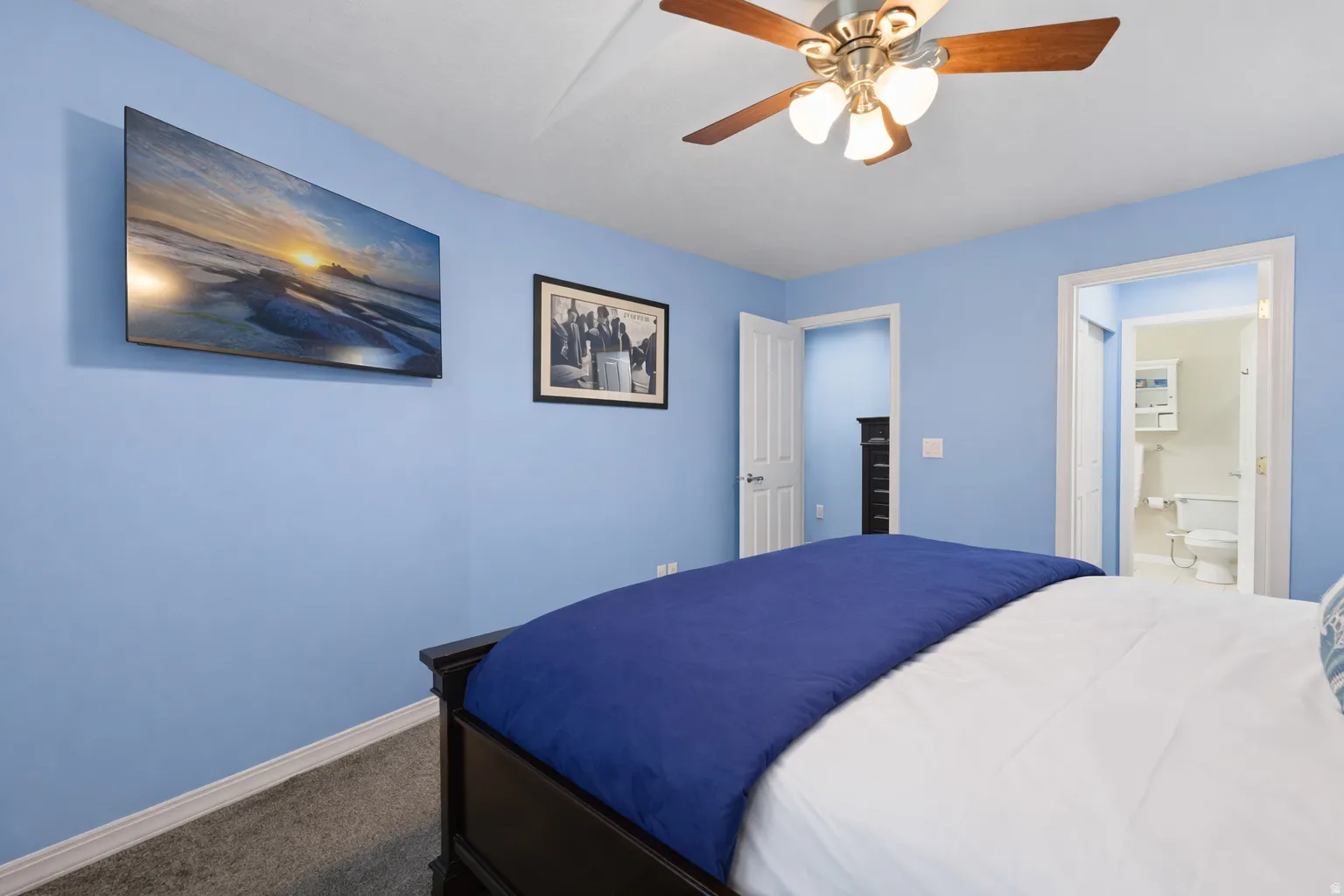 Primary bedroom with dark colored carpet, ensuite bath, a ceiling fan, and a spacious closet
