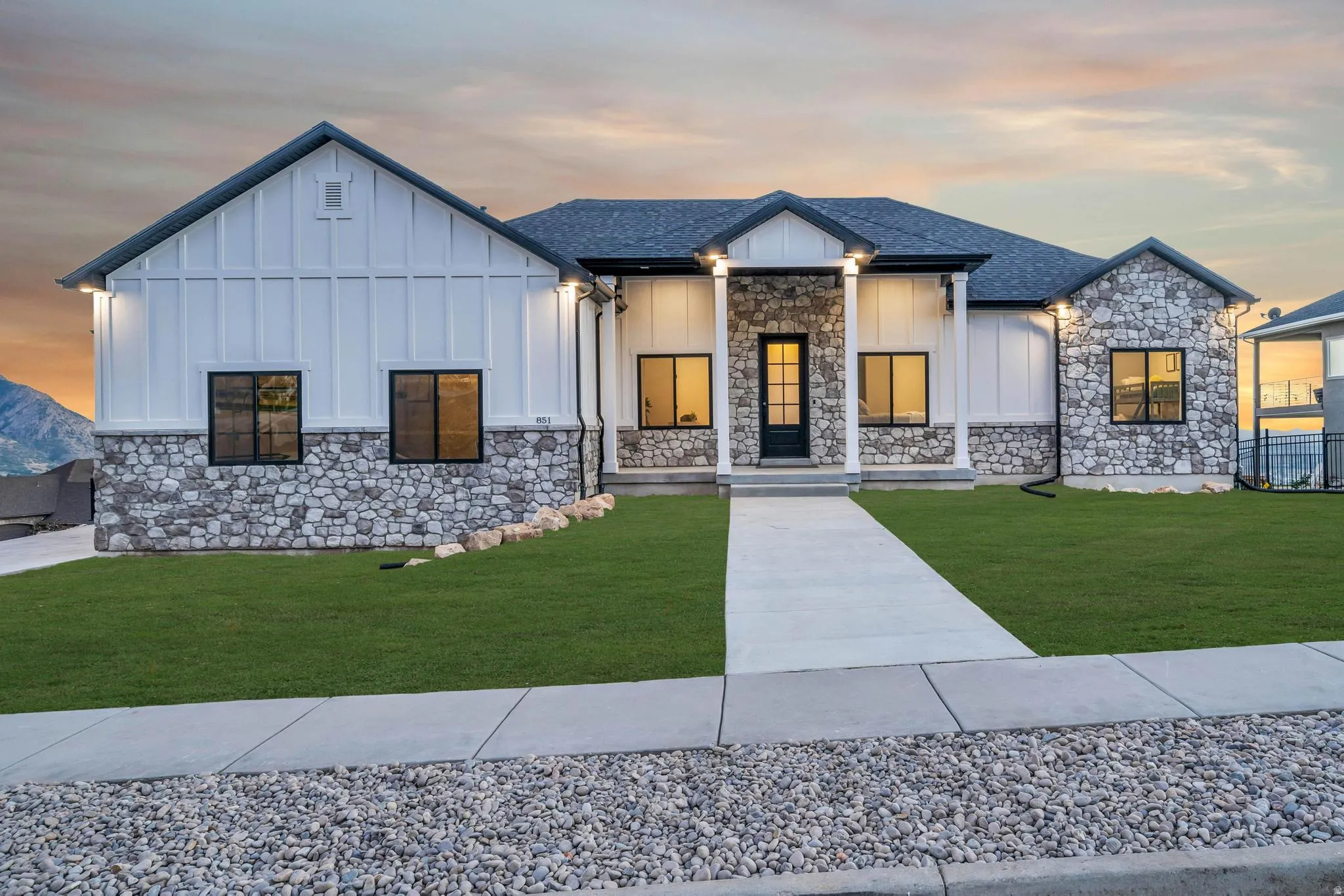Modern farmhouse style home with board and batten siding, covered porch, a lawn, stone siding, and roof with shingles