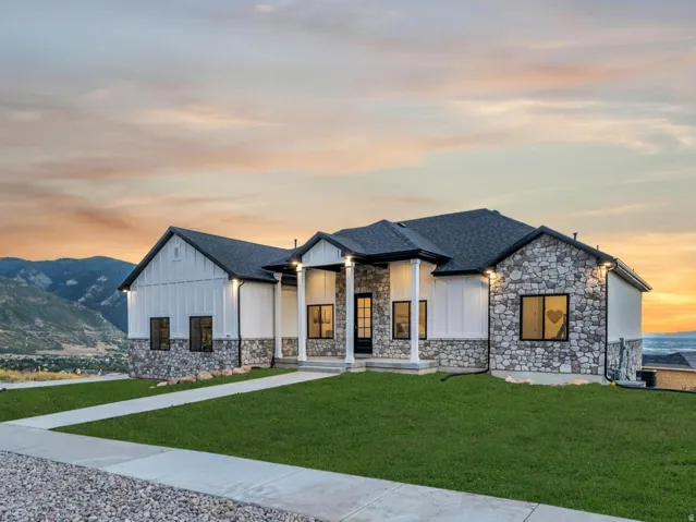 Modern inspired farmhouse featuring a lawn, board and batten siding, a mountain view, a shingled roof, and stone siding