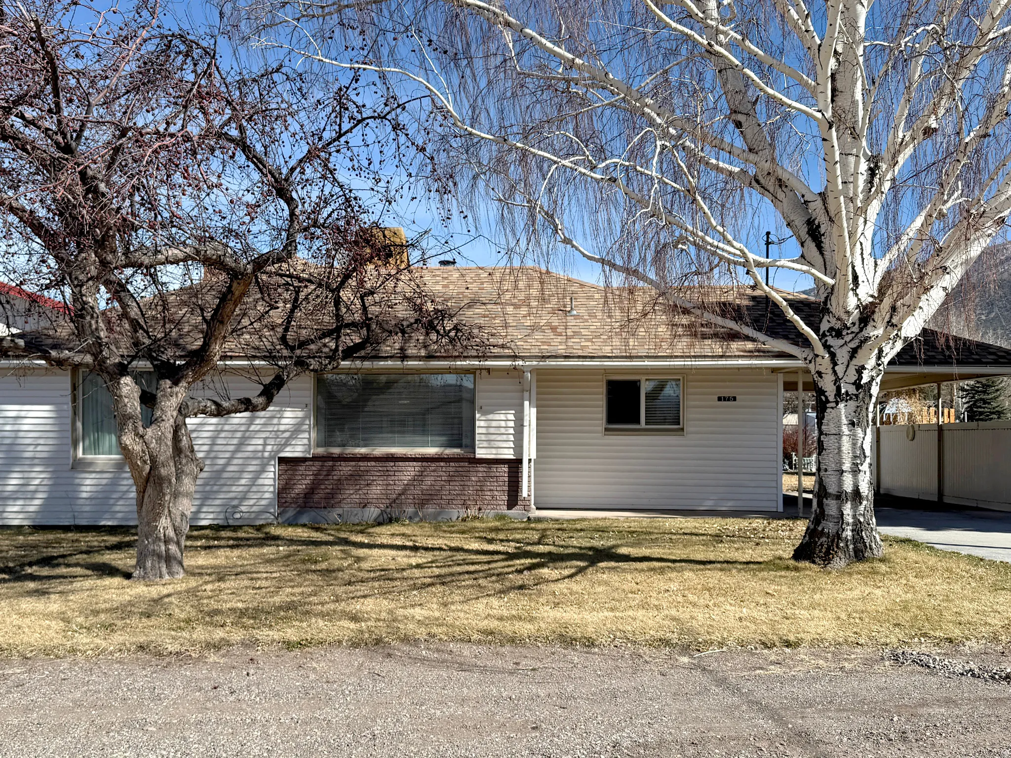 Ranch-style house featuring roof with shingles, a carport, a front yard, and brick siding