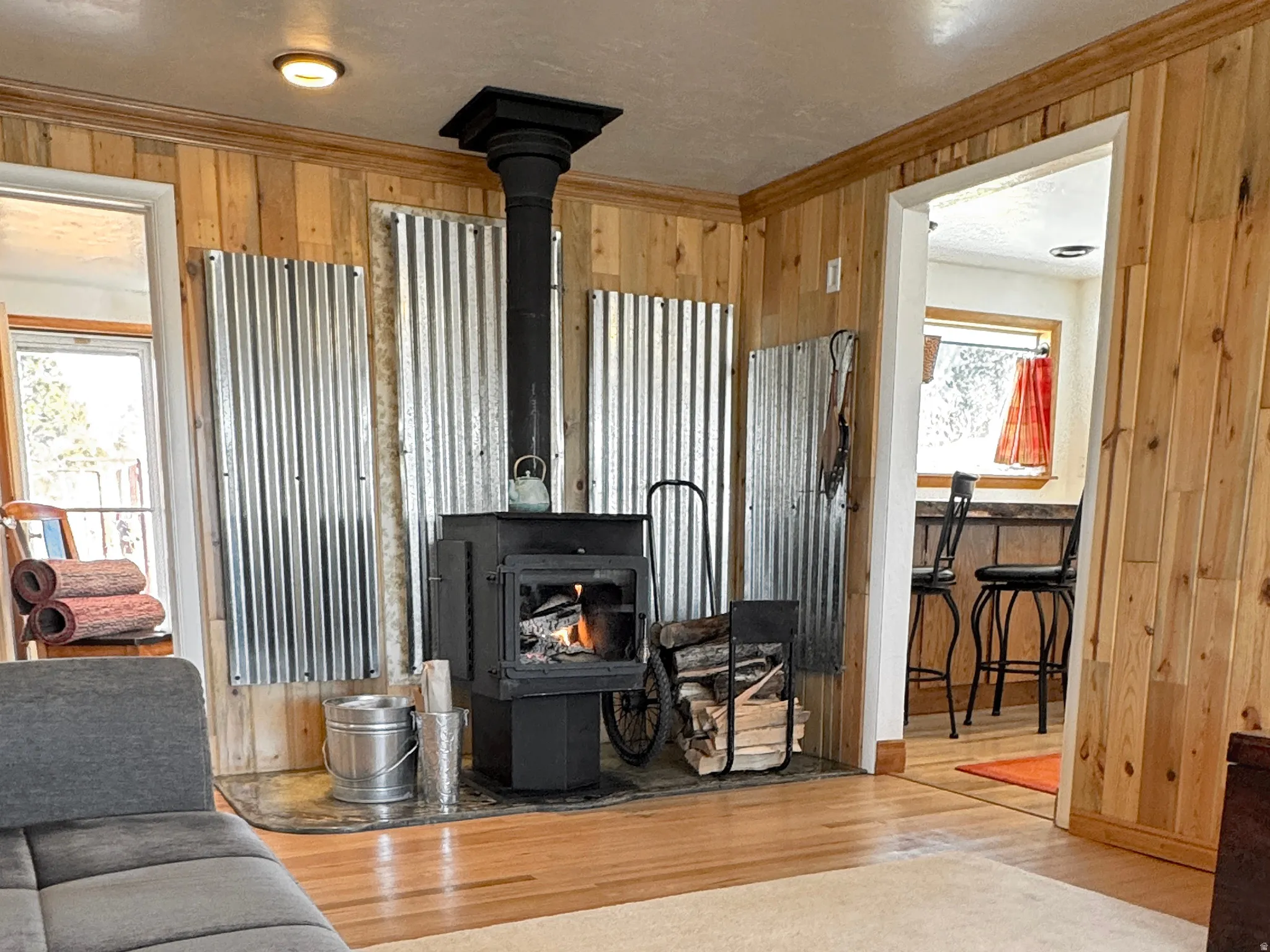 Living room with wood walls, a wood stove, wood finished floors, and crown molding