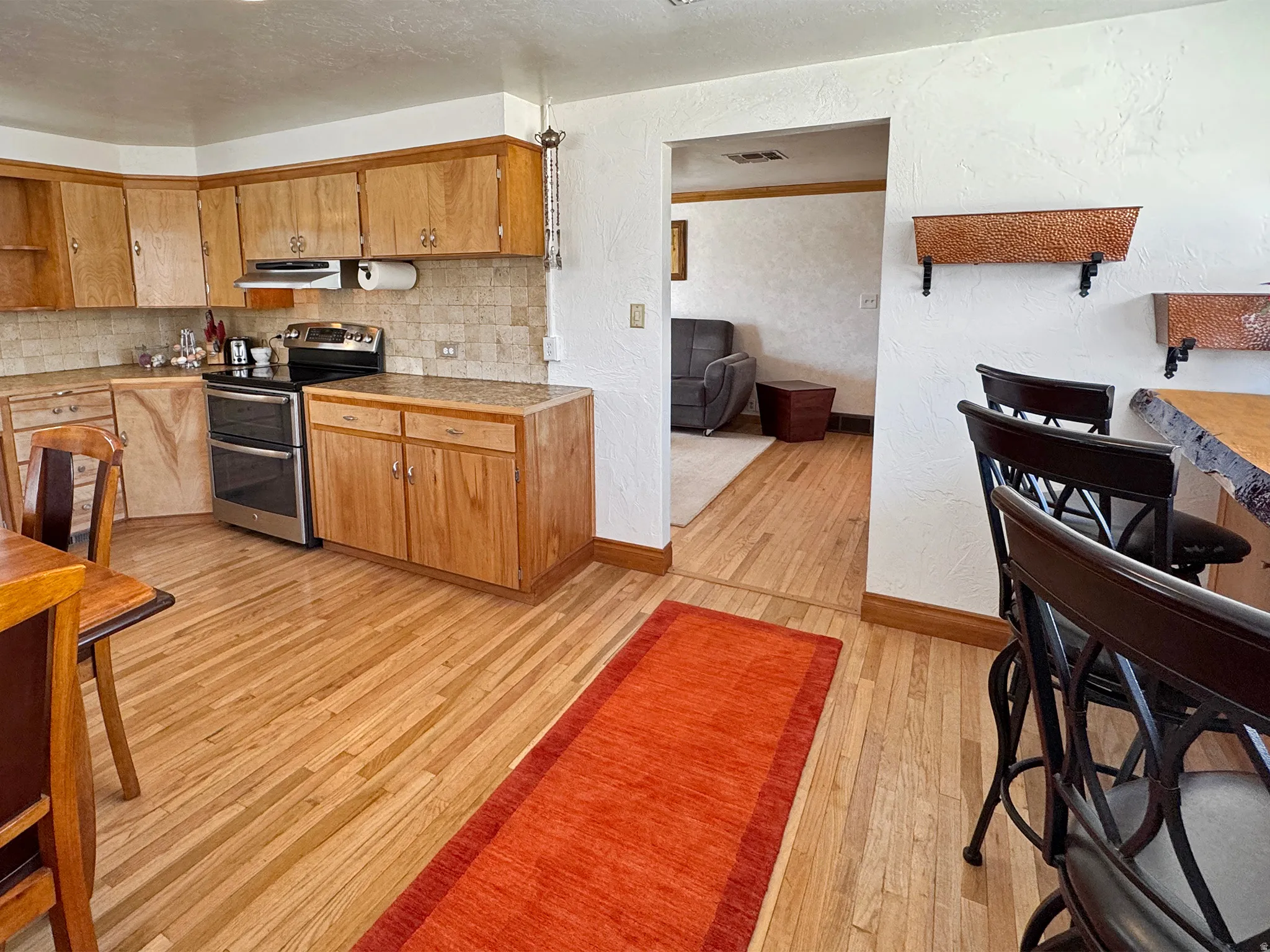 Kitchen featuring a textured wall, range with two ovens, light wood-style floors, wood finish cabinetry, and tasteful backsplash