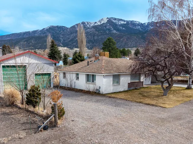 View of side of home featuring gravel driveway, an outbuilding, a mountain view, a chimney, and a shingled roof