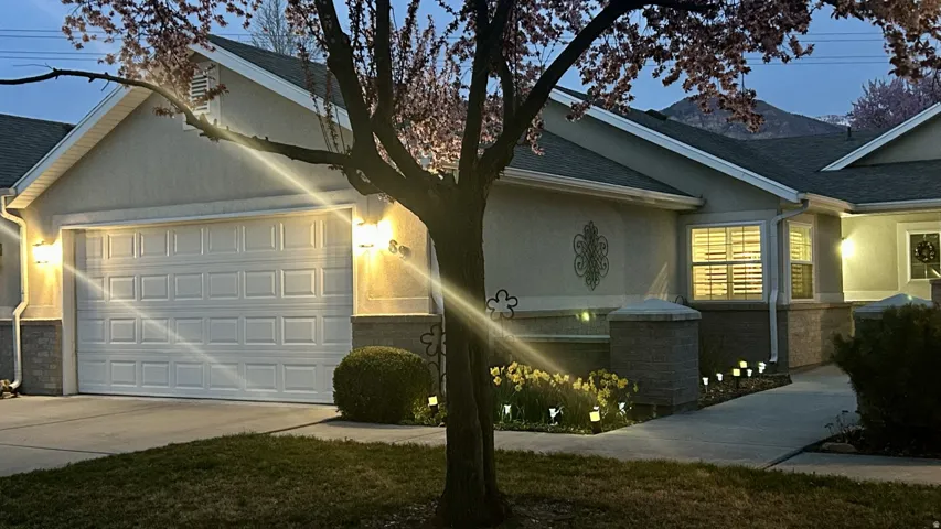 View of front of home with stucco siding, an attached garage, roof with shingles, driveway, and stone siding
