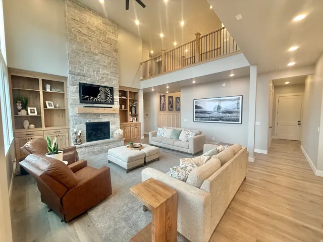 Living area with a high ceiling, a stone fireplace, light wood-style flooring, built in shelves, and recessed lighting