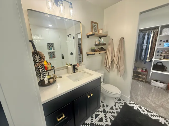 Full bath featuring vanity, a walk in closet, light tile patterned flooring, and a stall shower