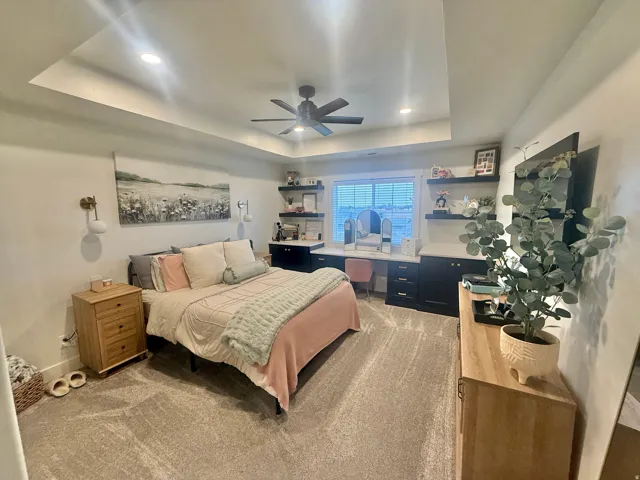 Bedroom featuring light colored carpet, ceiling fan, a tray ceiling, recessed lighting, and an office area