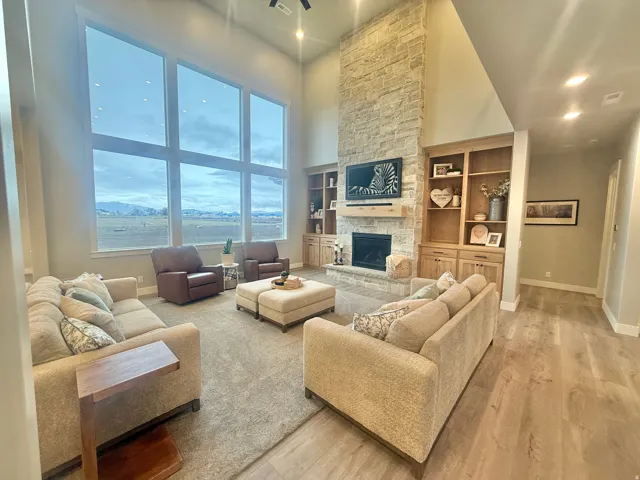 Living area featuring a high ceiling, recessed lighting, a stone fireplace, light wood-type flooring, and built in shelves