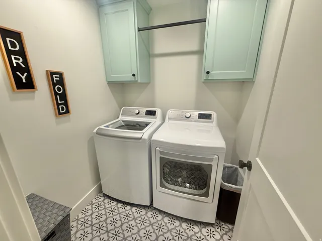 Laundry area featuring washing machine and dryer, cabinet space, and light tile patterned floors