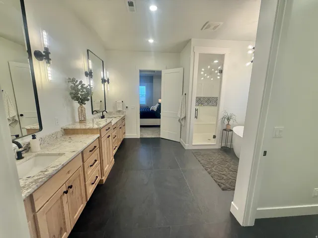 Ensuite bathroom with double vanity, a stall shower, a soaking tub, dark tile patterned flooring, and recessed lighting