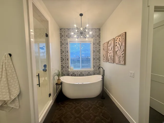 Bathroom with dark tile patterned floors, a shower stall, a soaking tub, and suspended lighting