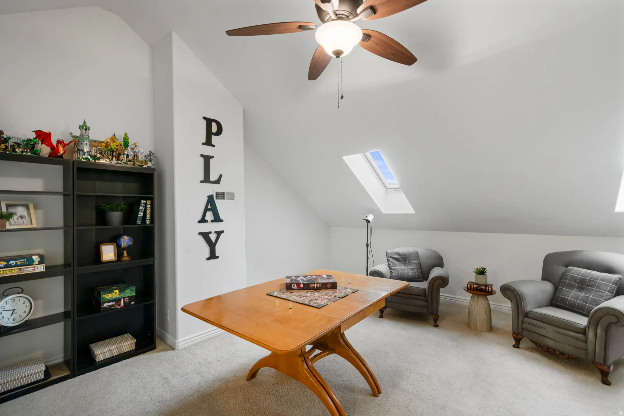 Loft with vaulted ceiling, a skylight, light carpet, and a ceiling fan