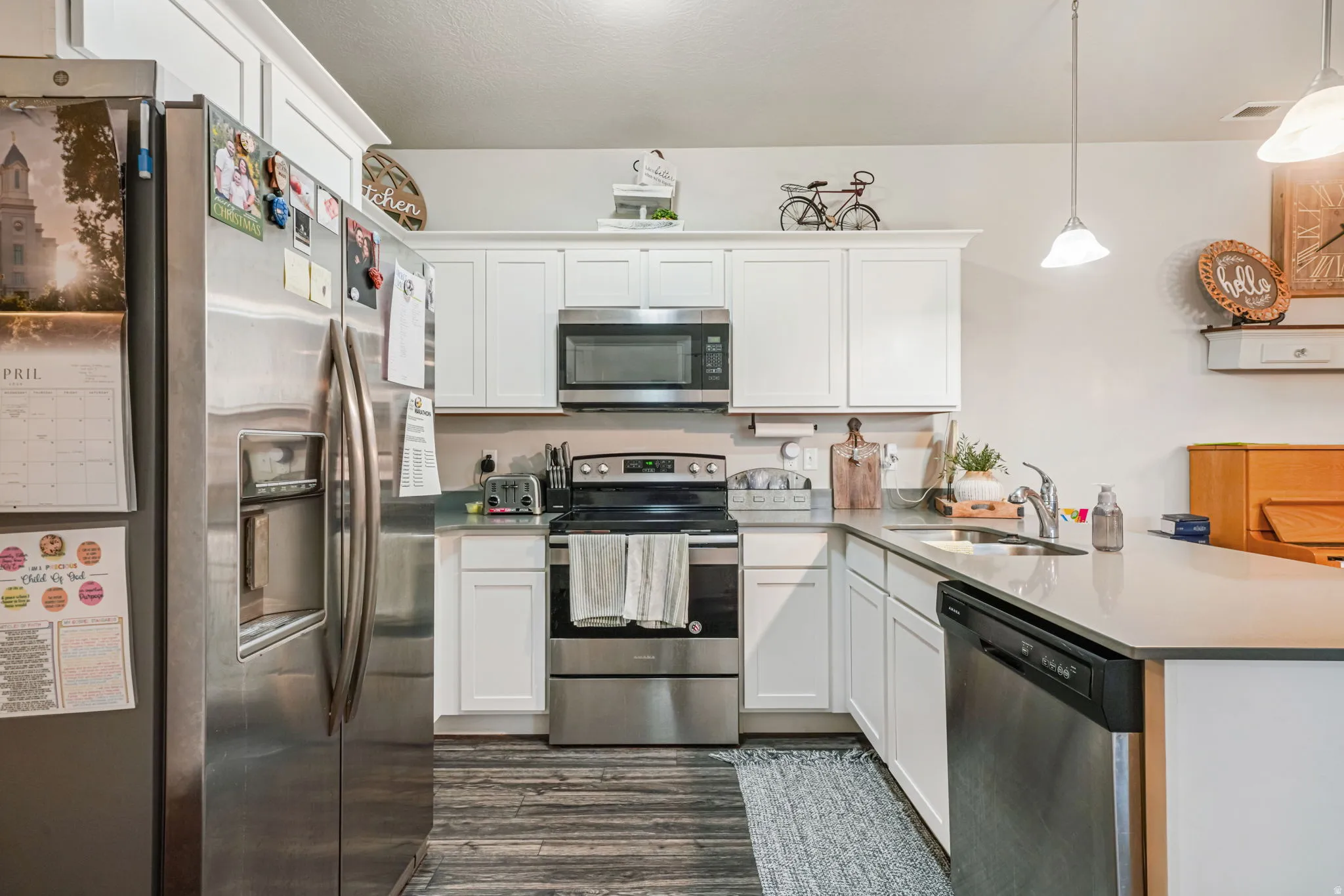 Kitchen featuring stainless steel appliances, white cabinetry, a peninsula, hanging light fixtures, and dark wood-style floors