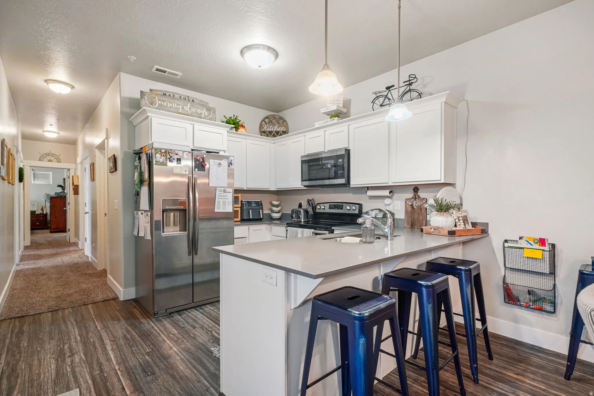 Kitchen featuring stainless steel appliances, a breakfast bar, white cabinets, a peninsula, and dark wood-style floors