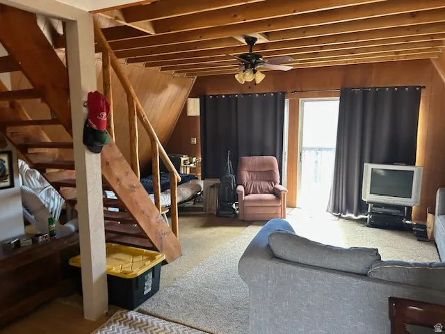 Living area featuring wood walls, a ceiling fan, and carpet floors