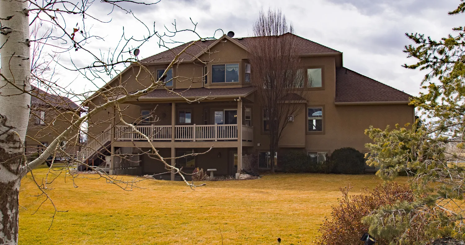 Back of house featuring a large yard, stucco siding, and a spacious covered deck.  Mature trees grace both the front and back yards.