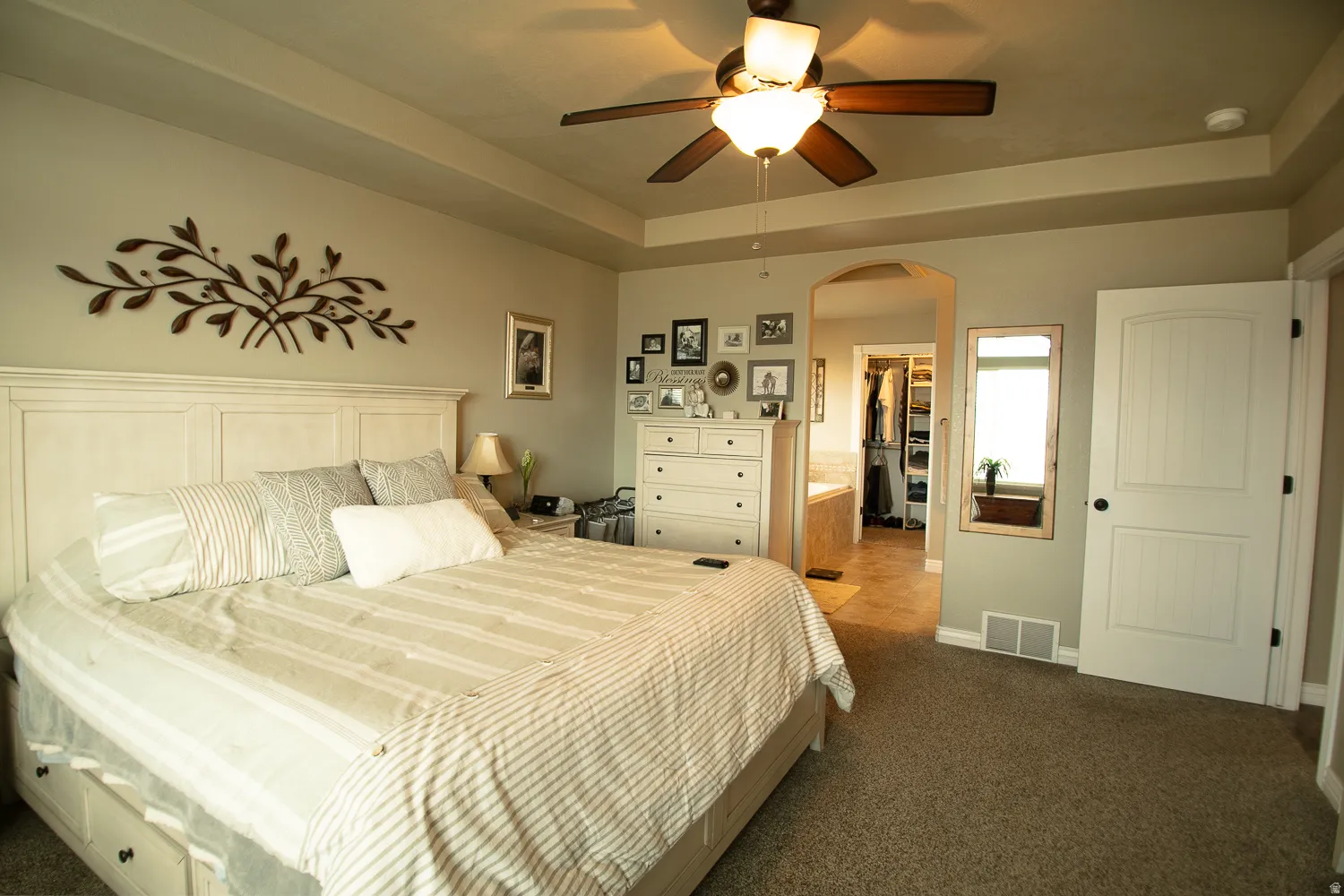 Bedroom featuring a raised ceiling, a spacious closet, dark carpet, arched walkways, and a ceiling fan