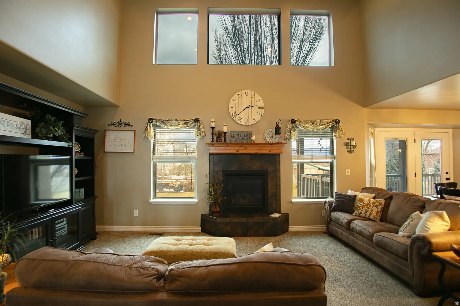 Carpeted living room featuring a tiled fireplace, healthy amount of natural light, and a high ceiling