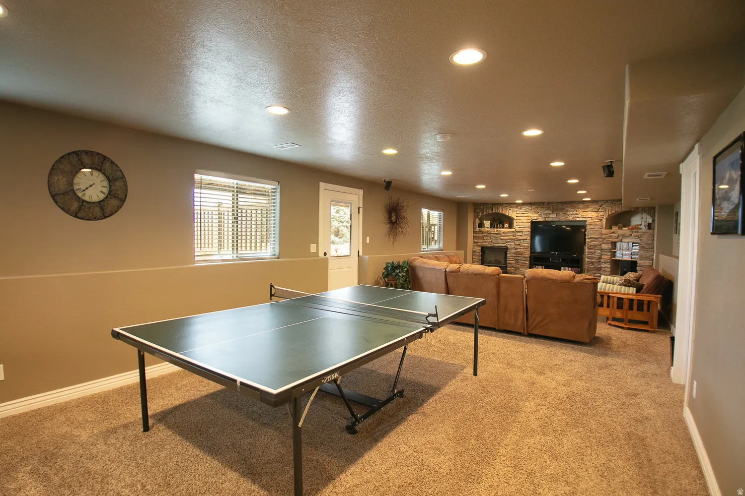 Downstairs recreation room featuring recessed lighting, daylight windows, and storage under the stairs with a walkout door to a patio and the beautiful backyard.