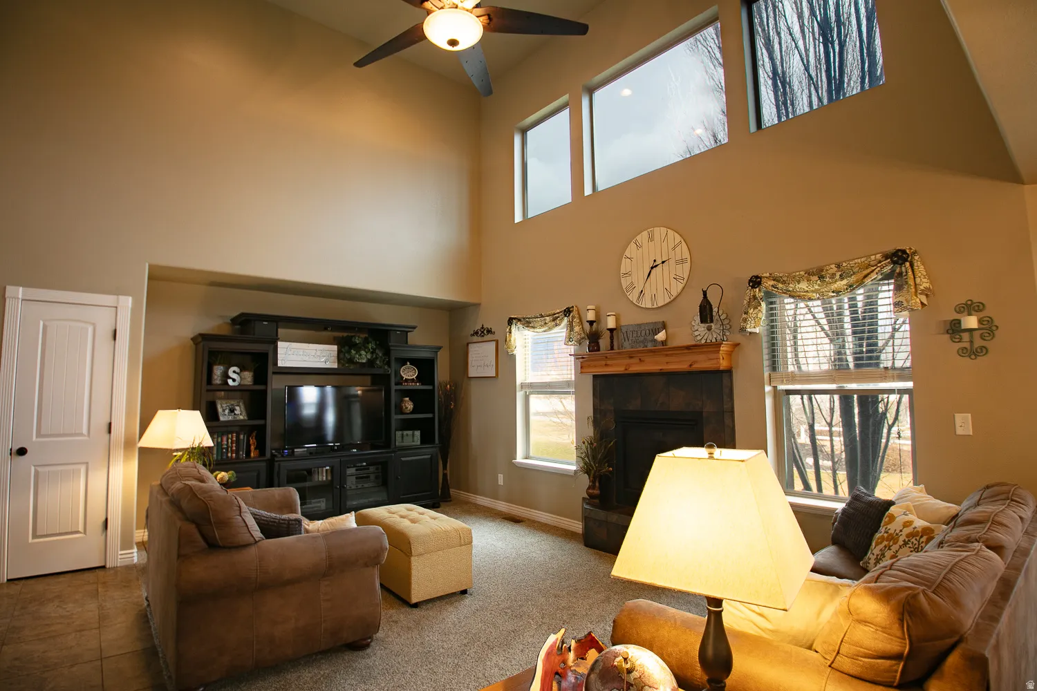 Living room featuring ceiling fan, a fireplace, a high ceiling, and carpet