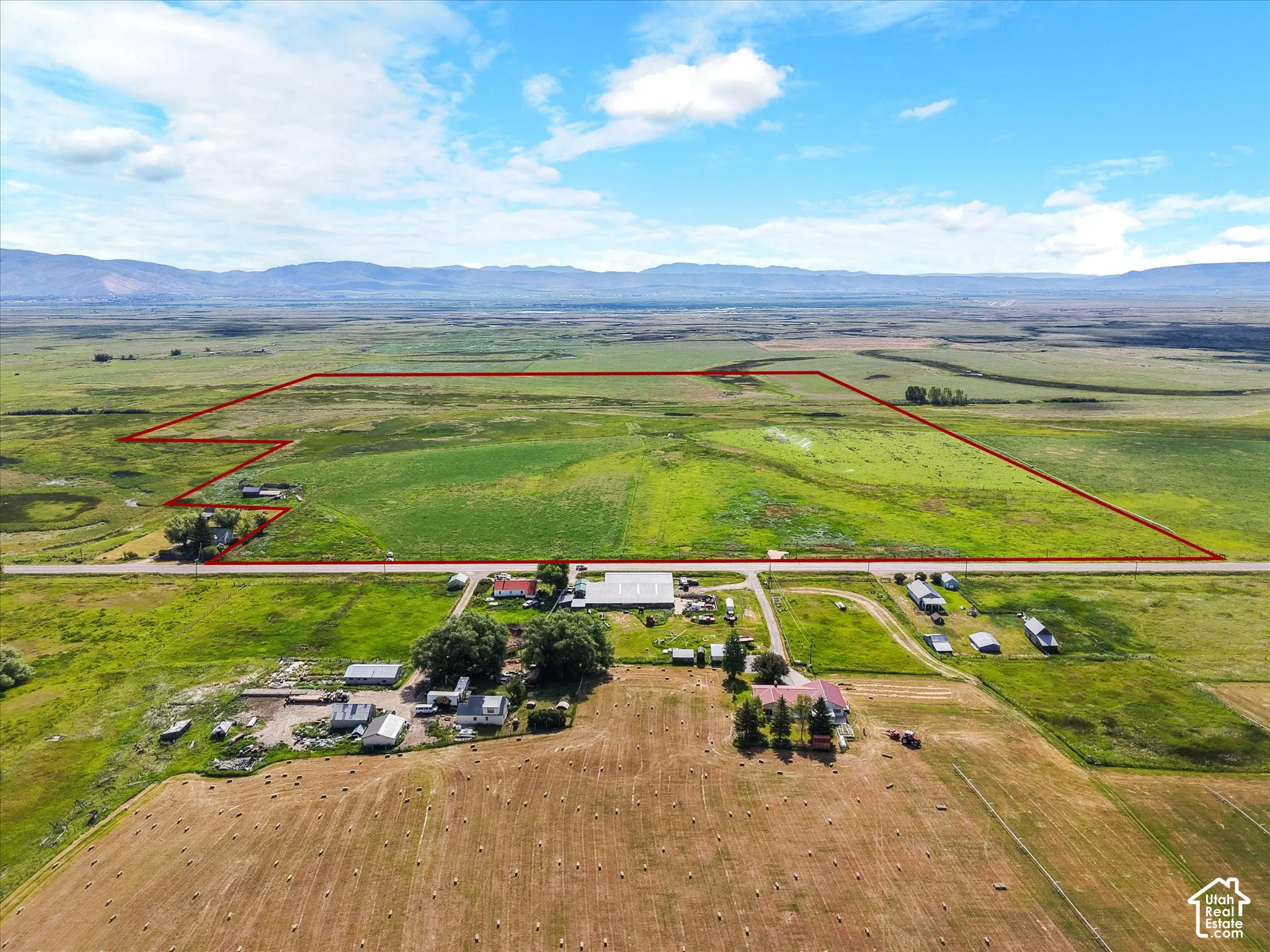 Expansive agricultural land featuring a mix of green fields and harvested hay bales, bordered by a road