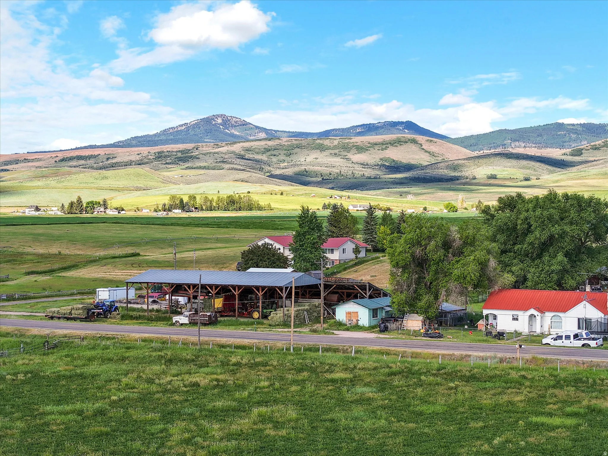 Expansive rural landscape featuring multiple structures, verdant fields, and distant mountains
