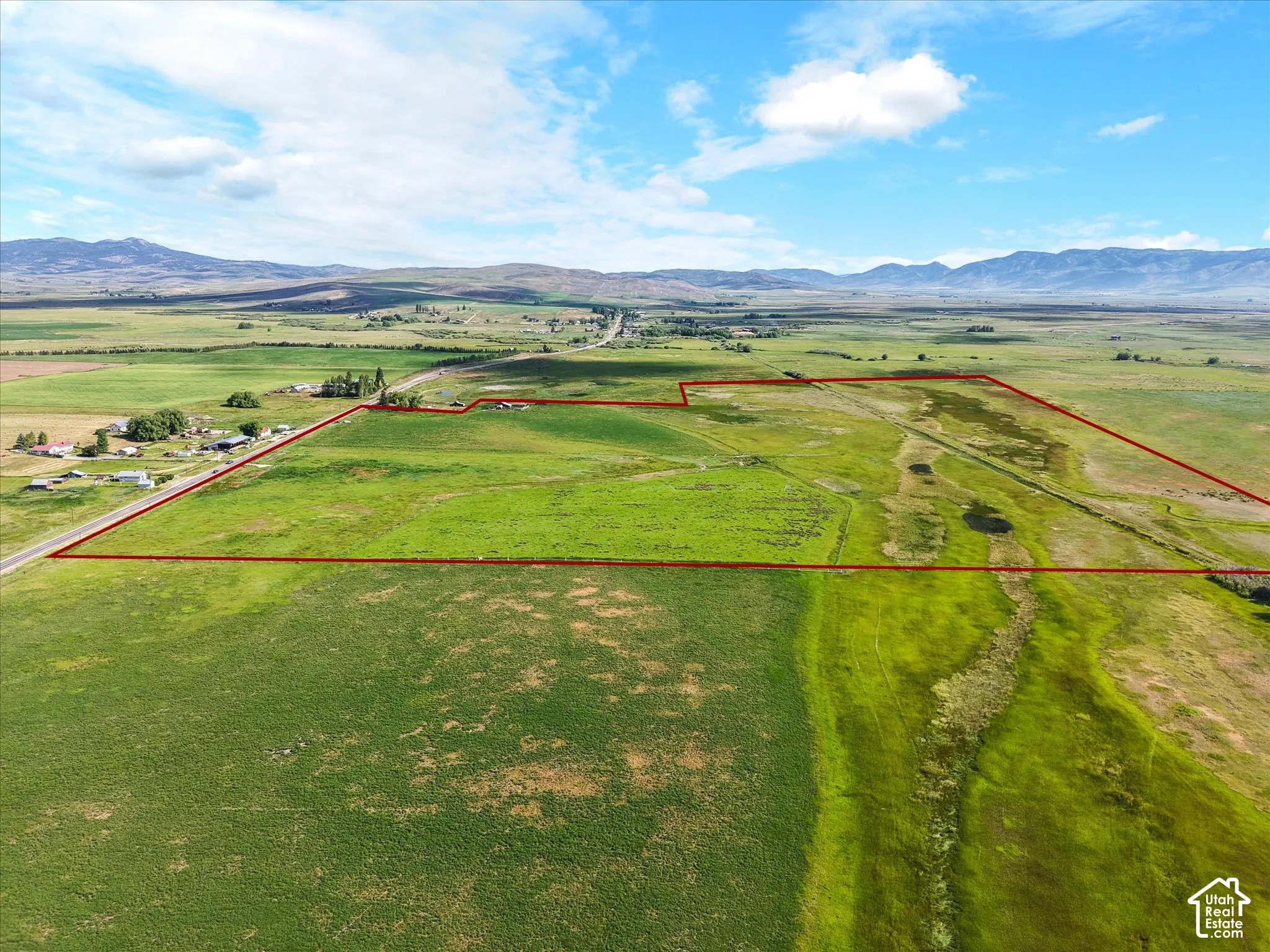Expansive green acreage featuring a clear boundary outline, road frontage, and distant mountain backdrops