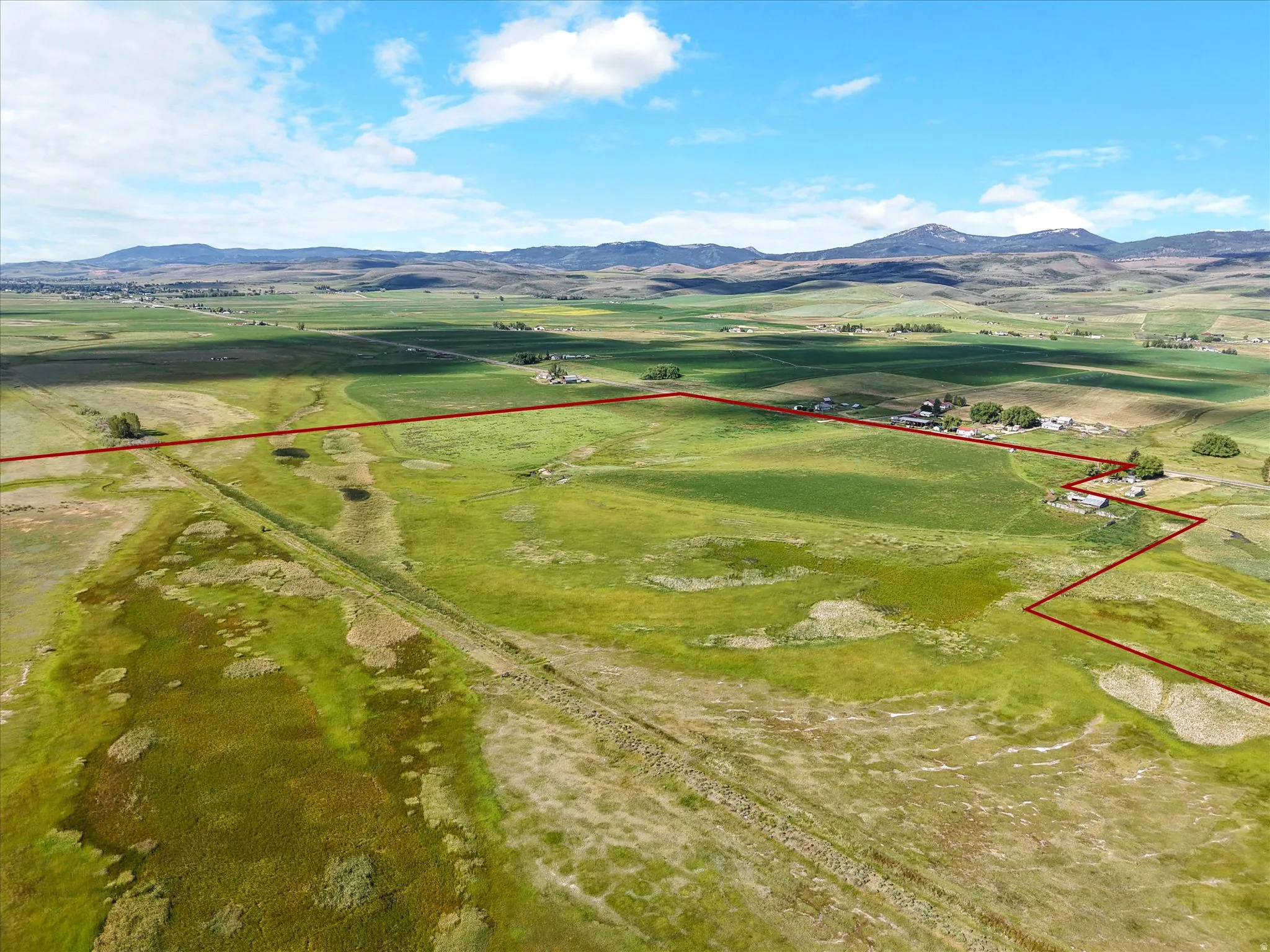 Expansive rural acreage featuring green pastures, distant mountains, and scattered structures