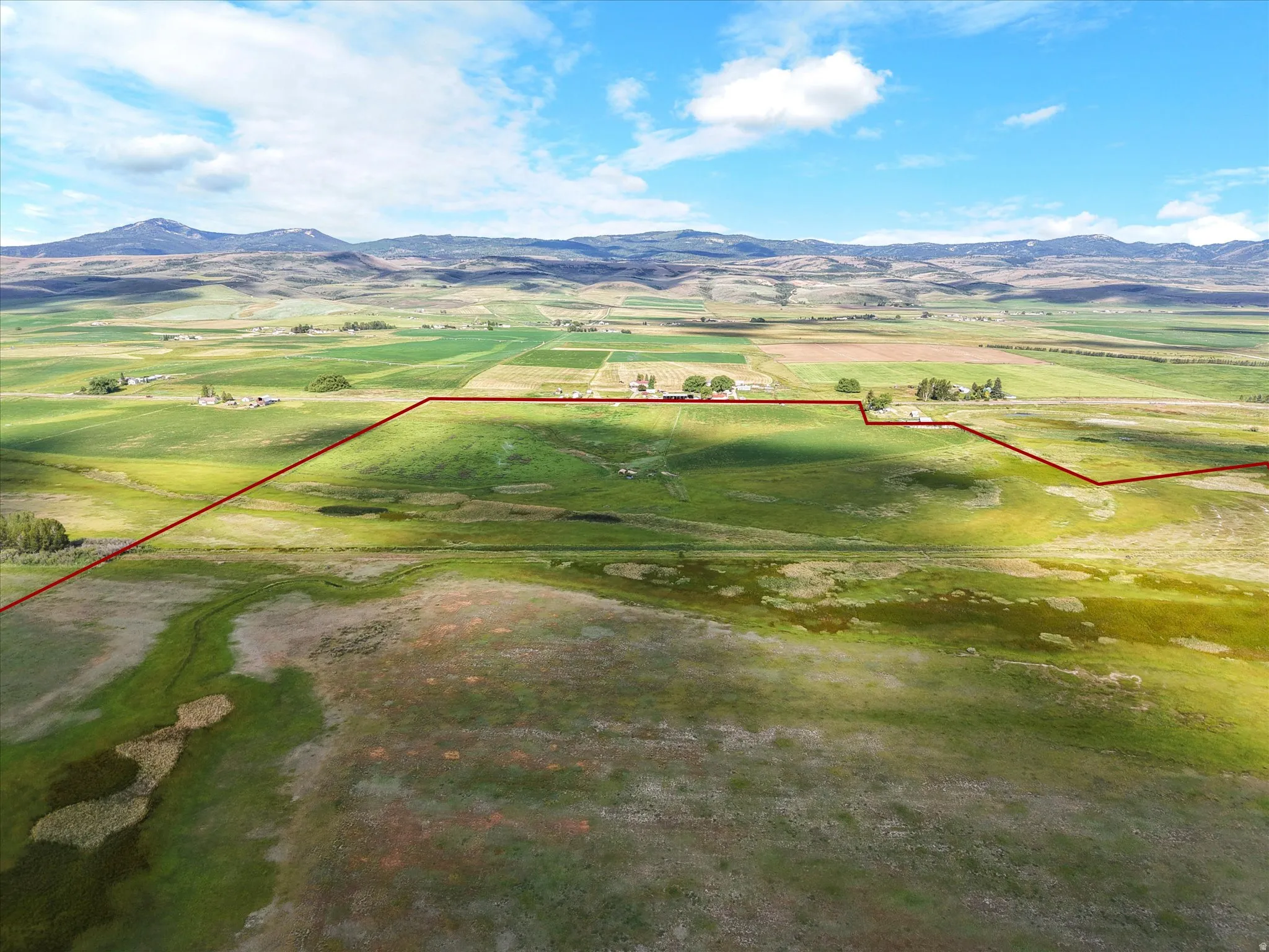 Expansive agricultural land featuring a diverse landscape of fields and wetlands, bordered by distant mountains